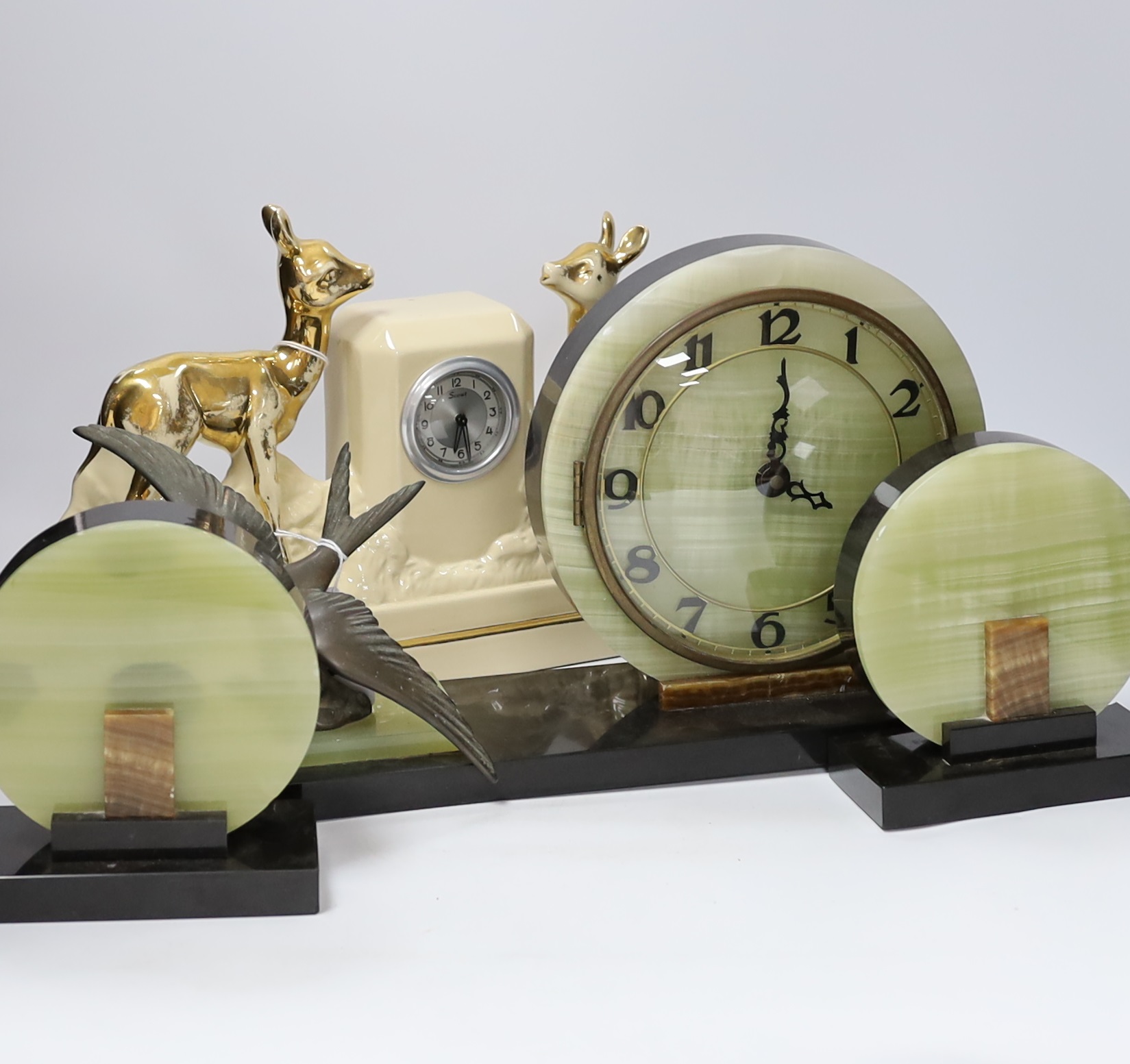 A French Art Deco green onyx clock garniture with bluebird spelter mount, together with two French ceramic mantel timepieces, largest 46cm wide